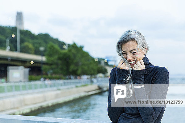 Cheerful woman in hooded shirt against sea on bridge
