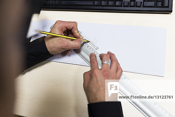 Ausgeschnittene Hände einer Ingenieurszeichnung auf Papier am Schreibtisch im Büro