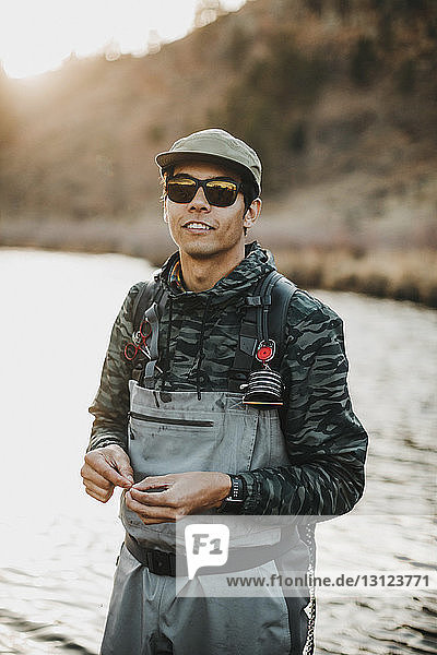 Portrait of male hiker wearing sunglasses standing in river against mountain