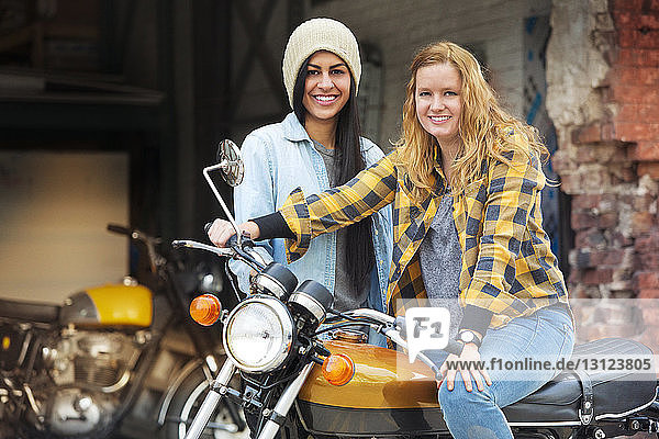 Porträt von fröhlichen Freundinnen mit Fahrrad vor einer Autowerkstatt