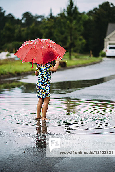 Rear view of girl holding umbrella while standing on road