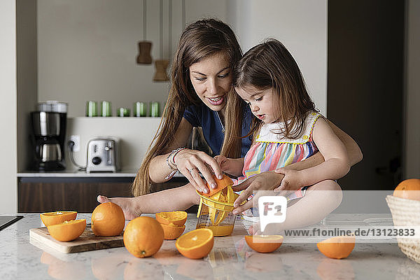 Mutter hilft Tochter beim Auspressen von Orangen auf Kücheninsel zu Hause