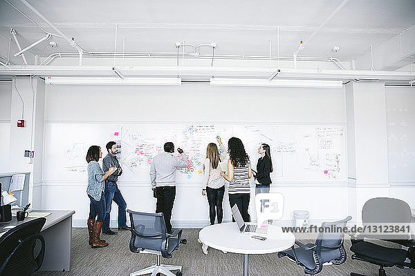 Geschäftsleute schreiben Notizen am Whiteboard während eines Brainstormings bei einer Besprechung im Büro