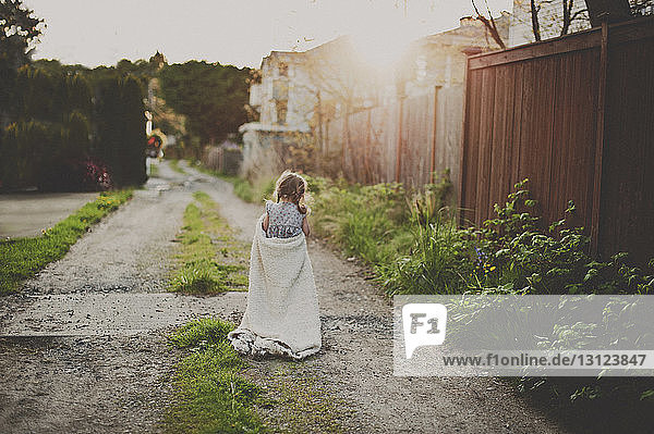 Rear view of girl holding blanket while walking on footpath