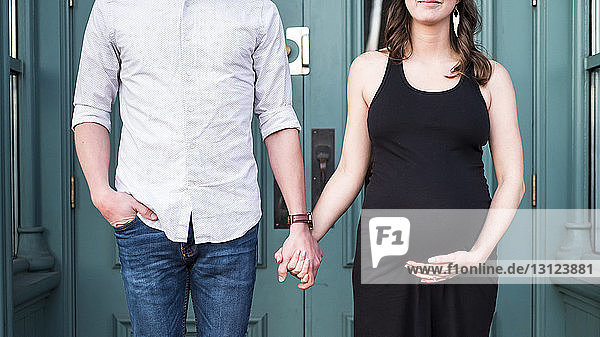 Midsection of couple holding hands while standing by door