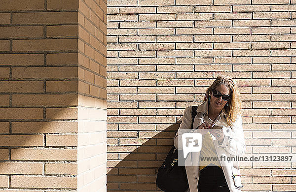 Geschäftsfrau benutzt Mobiltelefon  während sie an einer Ziegelmauer steht