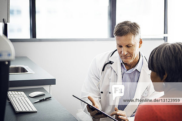 Male doctor showing report on tablet computer to patient in clinic