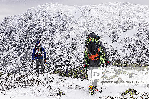 Rear view of backpackers standing on snowcapped Mountain during winter