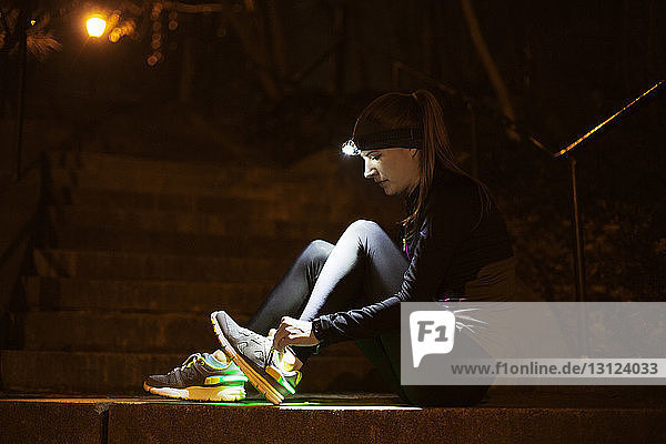 Seitenansicht einer jungen Frau mit beleuchtetem Scheinwerfer  der die Schnürsenkel auf den Stufen bindet