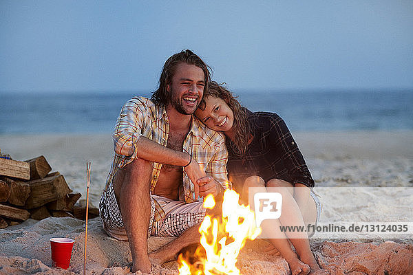 Fröhliches Paar sitzt am Strand am Lagerfeuer im Sand