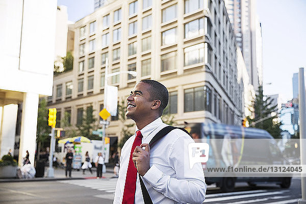 Smiling businessman looking away while standing on city street