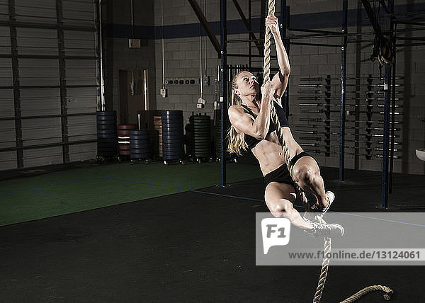 Confident athlete climbing rope at gym