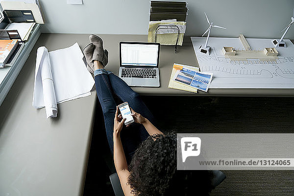 Weitwinkelansicht einer Geschäftsfrau  die ein Smartphone benutzt  während sie sich am Schreibtisch im Büro entspannt