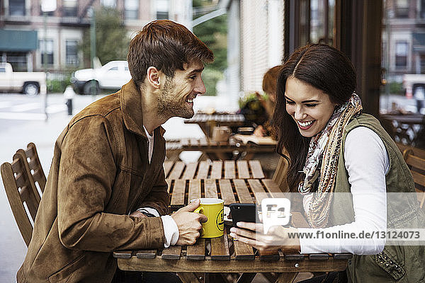 Mann sieht seine Freundin im Café mit dem Handy an
