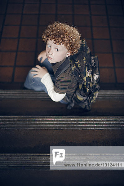 Hochwinkelporträt eines Jungen  der auf Stufen in der Schule sitzt