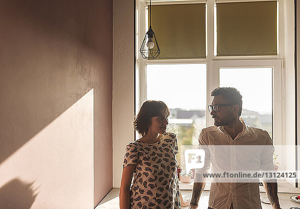Man and PRegnant woman looking face to face while standing against window at home