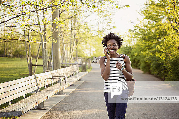 Fröhliche Frau benutzt Smartphone  während sie auf einem Fußweg im Park spazieren geht