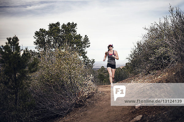 Full length of sporty woman running on mountain against sky