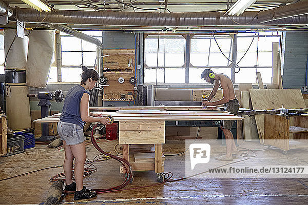 Tischler in voller Länge beim Schleifen von Holzbohlen in der Werkstatt