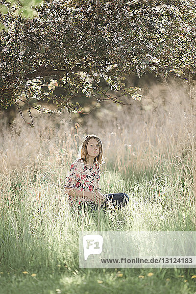 Portrait of girl sitting on grassy field under tree