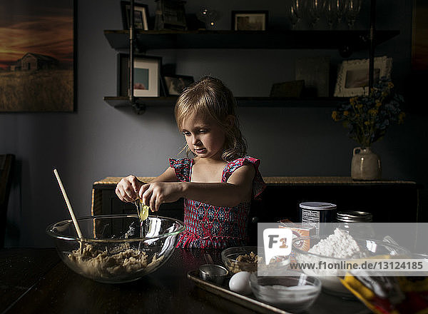 Mädchen zerbricht Eier in Schüssel auf dem heimischen Tisch