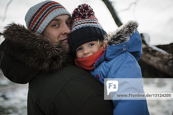 Portrait of father carrying daughter while standing outdoors in winter