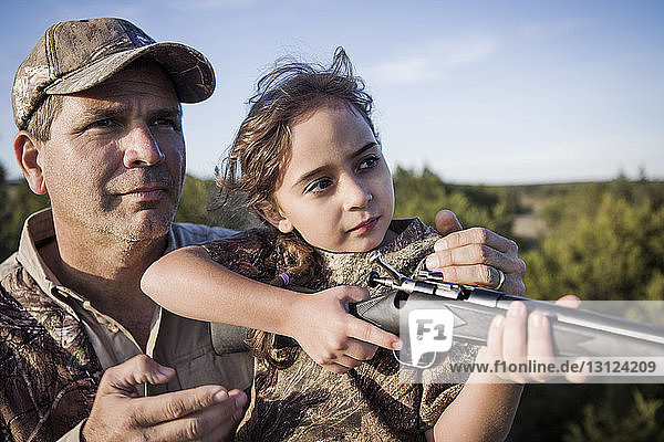 Zuversichtliches Mädchen zielt Gewehr mit Vater auf dem Feld