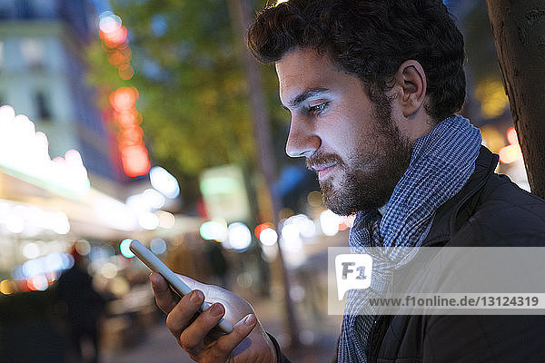 Seitenansicht eines Mannes mit einem Smartphone in einer beleuchteten Stadt bei Nacht