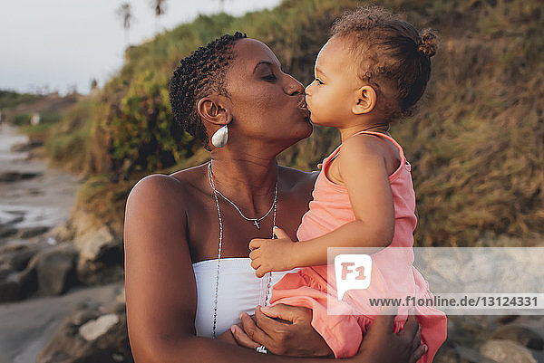 Mutter küsst Tochter  während sie am Strand steht