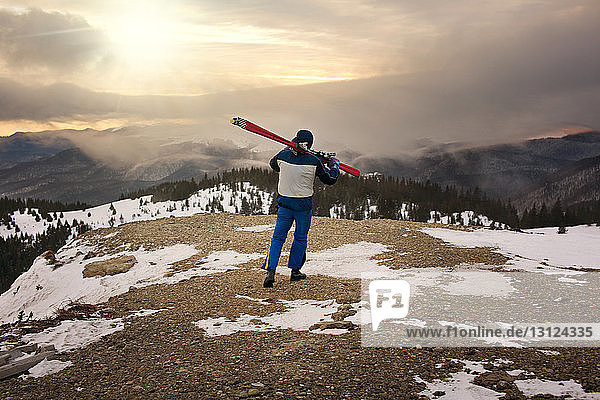 Rückansicht eines Mannes  der Skier beim Gehen am Berg trägt