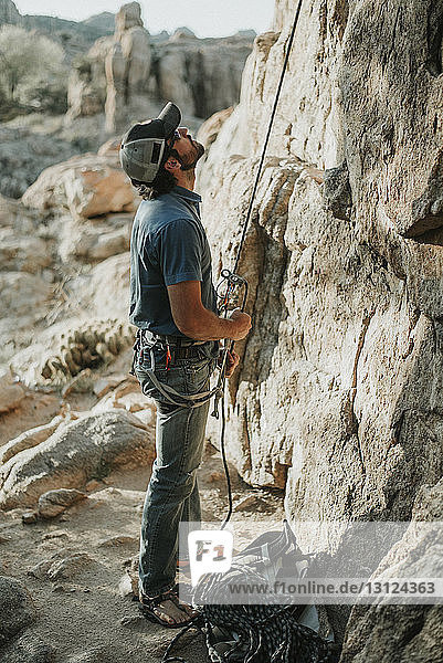 Hiker looking up while holding climbing rope by rock formation