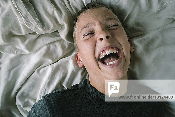 Hochwinkelaufnahme eines Jungen  der lacht  während er zu Hause auf dem Bett liegt