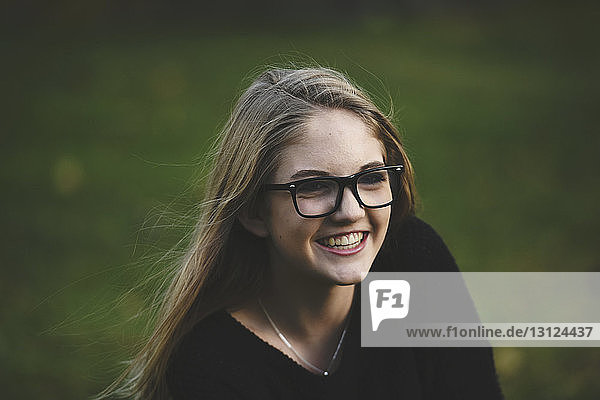 Hochwinkelansicht eines lächelnden Teenager-Mädchens  das wegschaut  während es auf einem Grasfeld im Hof sitzt