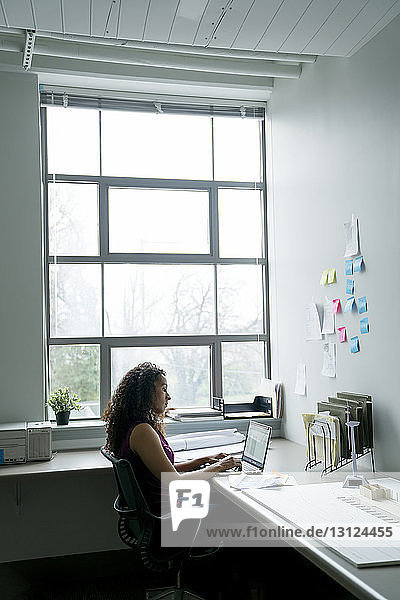 Seitenansicht einer Geschäftsfrau mit Laptop-Computer am Schreibtisch im Büro