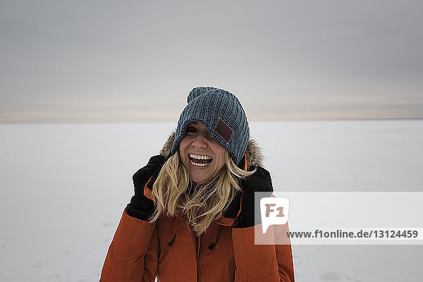 Glückliche Frau steht auf schneebedeckter Landschaft vor bewölktem Himmel