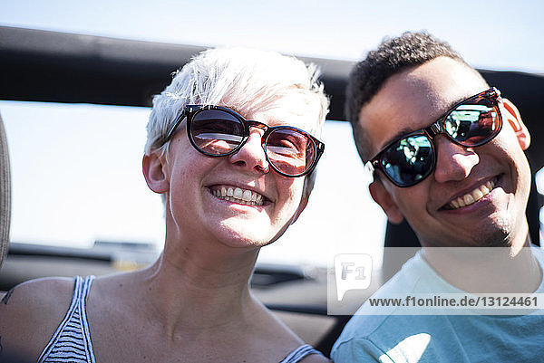 Porträt von lächelnden Freunden mit Sonnenbrille  die im Geländewagen gegen den Himmel fahren