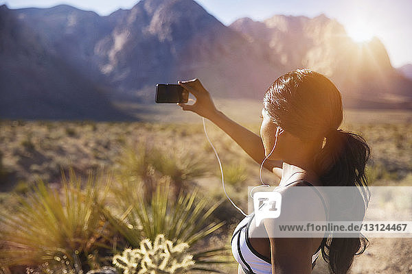 Woman photographing through phone while standing on field against mountains