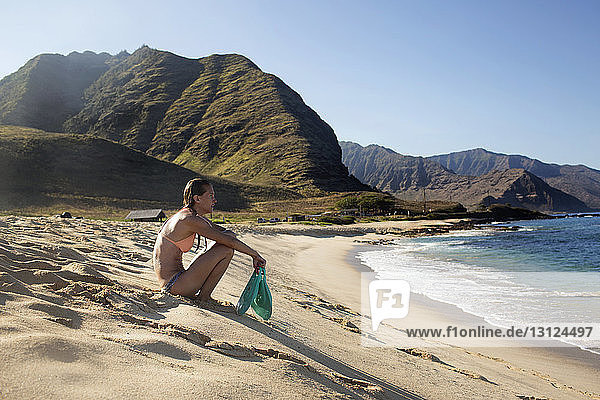 Seitenansicht einer Frau  die am Strand sitzend Tauchflossen hält