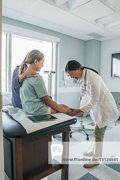 Pediatrician examining girl's knee joint while standing in medical examination room