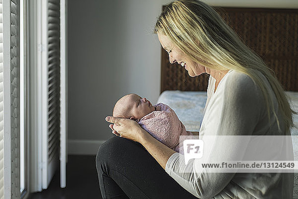 Seitenansicht einer glücklichen Mutter  die ihre neugeborene Tochter betrachtet  während sie sie zu Hause trägt