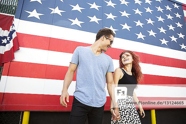 Young couple holding hands while standing against American flag