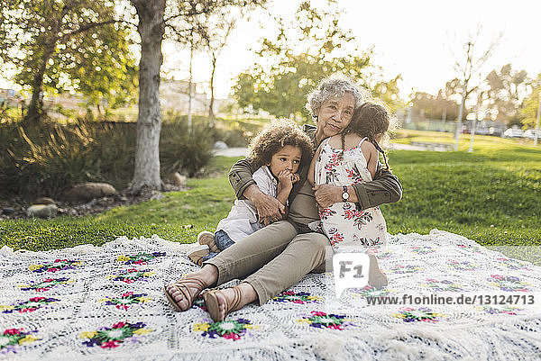 Porträt einer Grossmutter  die ihre Enkel auf einer Picknickdecke im Park umarmt