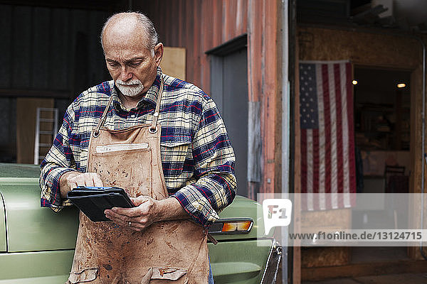 Leitender Handwerker benutzt digitales Tablett  während er vor der Werkstatt steht