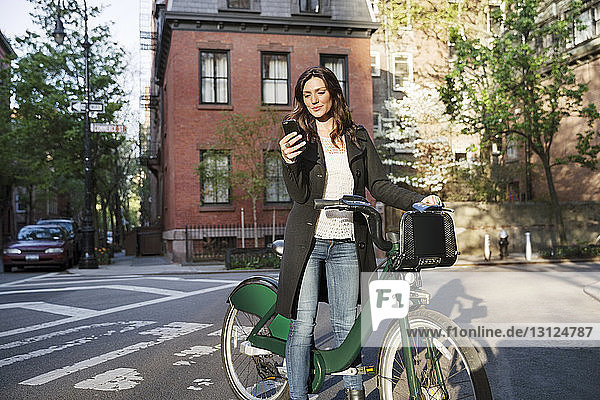 Junge Frau benutzt ein Smartphone  während sie mit dem Fahrrad auf der Straße steht