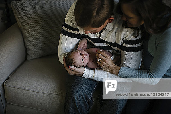 High angle view of parents playing with newborn son while sitting on sofa at home