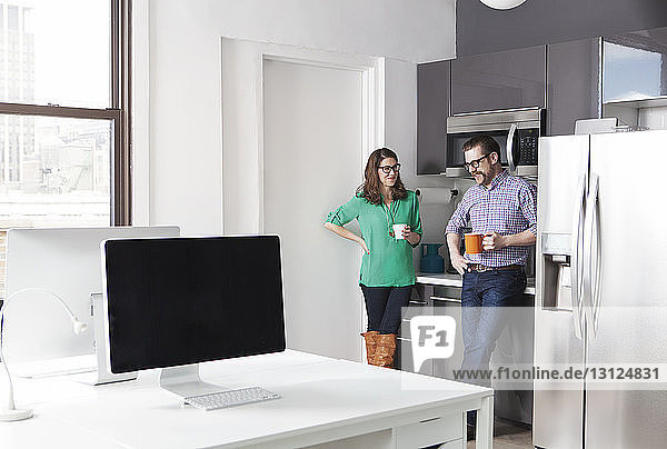 Creative business colleagues holding coffee mugs while discussing in office