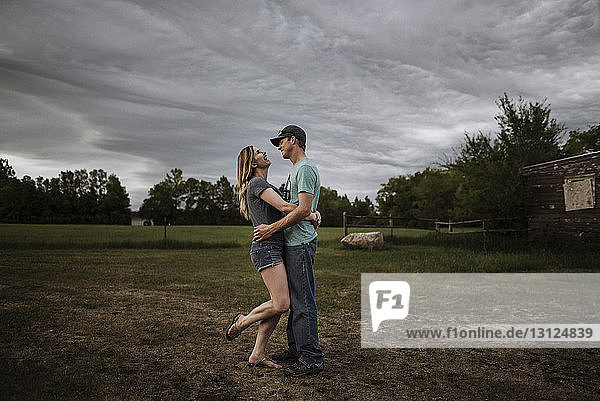 Side view of couple standing on field against cloudy sky