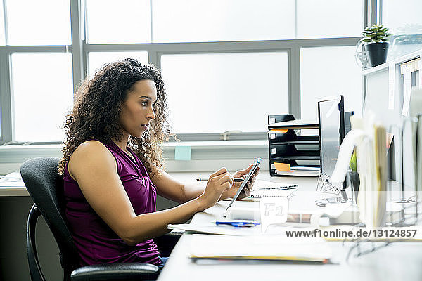 Seitenansicht einer Geschäftsfrau mit Grafiktablett am Schreibtisch im Büro