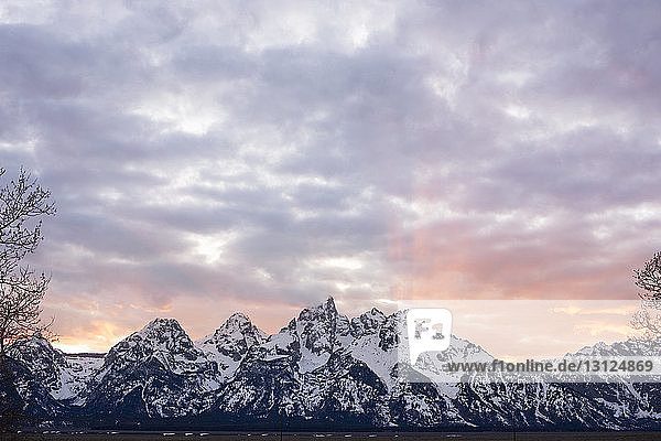 Idyllischer Blick auf schneebedeckte Berge vor bewölktem Himmel bei Sonnenuntergang