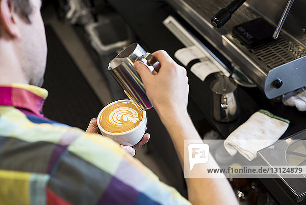 High angle view of barista pouring milk in coffee while making frothy drink at cafe